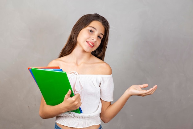 Jovem garota caucasiana com notebooks nas mãos apontando para espaço livre para textodia do estudante voltar para a escola