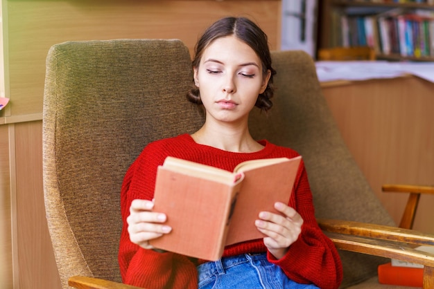 Jovem garota caucasiana está interessada em ler sentada na biblioteca