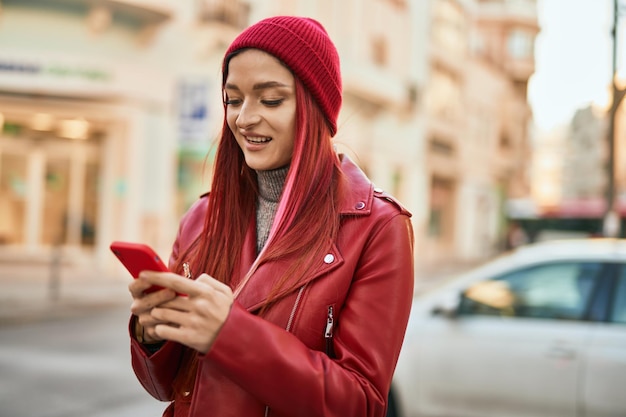 Jovem garota caucasiana sorrindo feliz usando smartphone na cidade