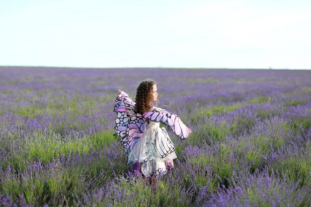 Jovem garota com cabelo comprido no campo de lavanda em vestido de borboleta