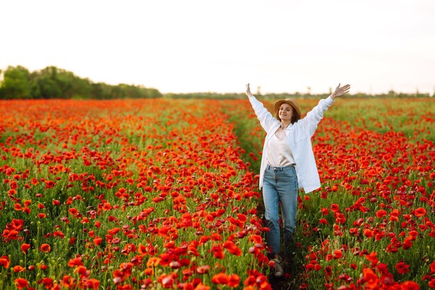 Foto jovem garota com chapéu posando no campo de papoulas retrato de garota encaracolada caminhando no campo de papoulas ao pôr-do-sol