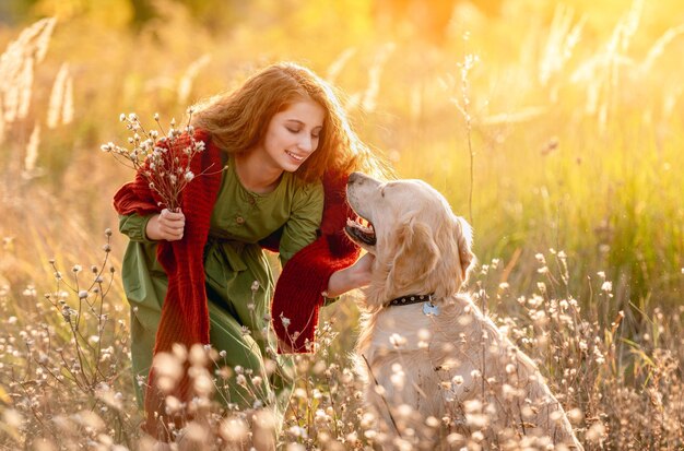 Jovem garota com flores de campo acariciando cão golden retriever no meio da natureza de outono