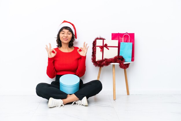 Jovem garota comemorando o natal sentada no chão, isolada em um fundo branco, mostrando um sinal de ok com os dedos