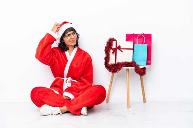 Jovem garota comemorando o Natal sentada no chão, isolada no fundo branco, tendo dúvidas e com expressão facial confusa