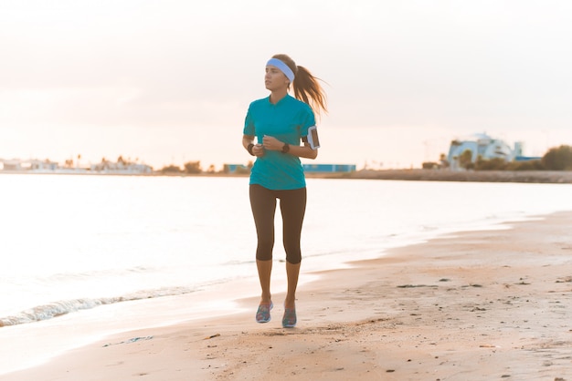 Jovem garota desportiva correndo na praia ao nascer do sol na manhã