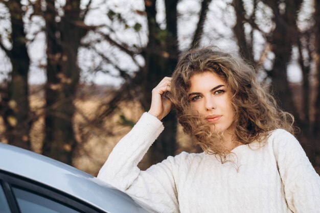 Foto jovem garota encaracolada com uma camisola branca contra o pano de fundo da natureza de outono e seu próprio carro