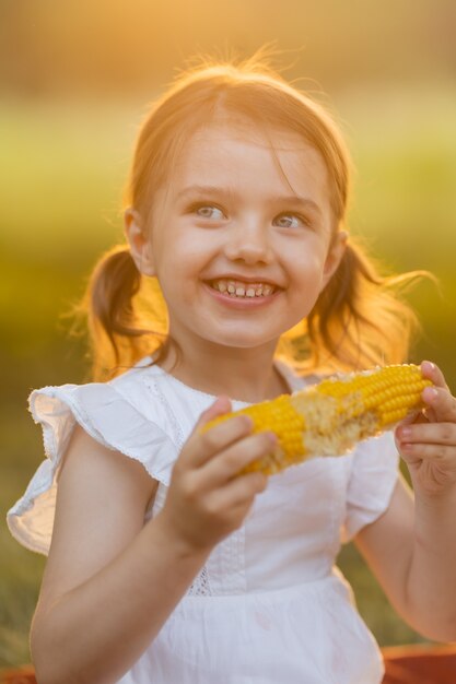 Jovem garota engraçada comendo milho cozido Criança no jardim garota comendo milho na espiga Alimentos sem OGM