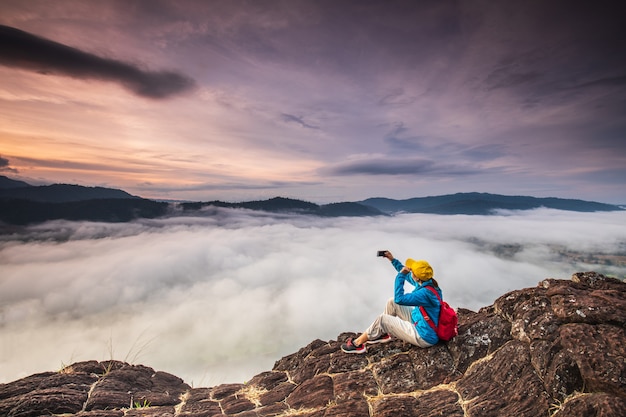 Jovem garota está tirando fotos do mar de névoa na alta montanha.