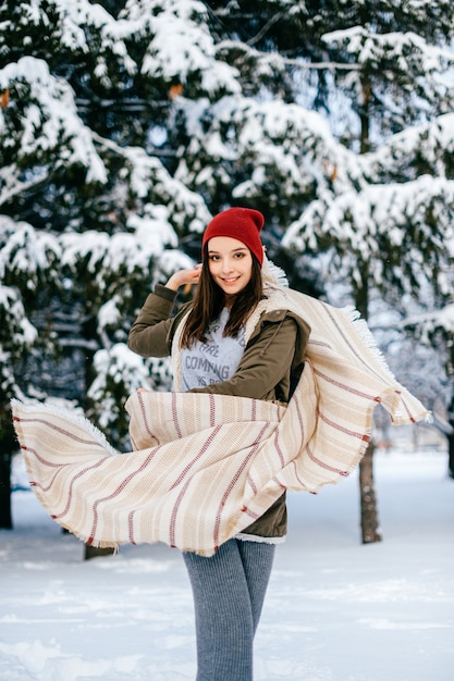 Jovem garota morena atraente posando com uma capa voadora na floresta de neve