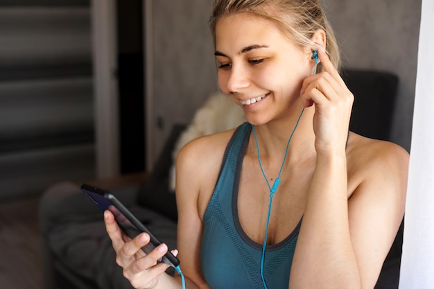 Jovem garota muito esportiva em casa ouve música em fones de ouvido no smartphone