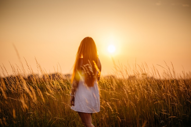 Jovem garota ruiva bonita em um campo ao pôr do sol