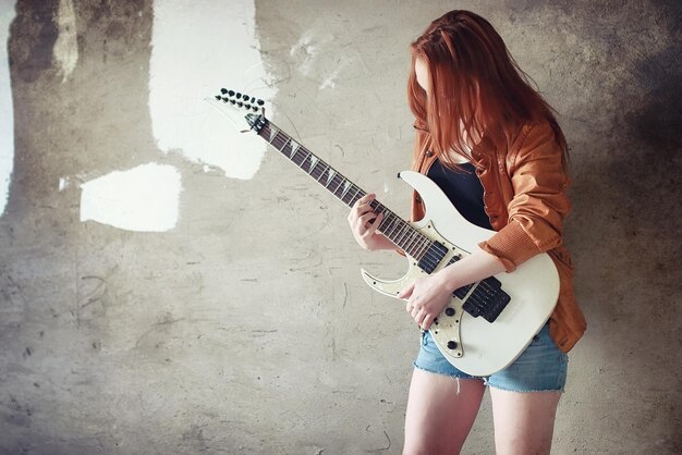 Jovem garota ruiva com guitarra elétrica. Menina do músico de rock em uma jaqueta de couro. Ela é uma bela cantora e intérprete de rock.