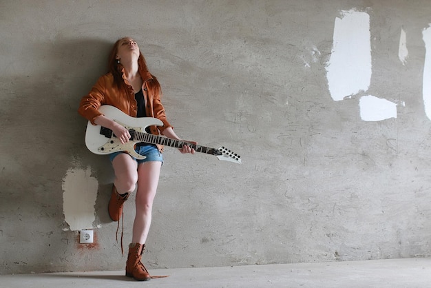 Jovem garota ruiva com guitarra elétrica. menina do músico de rock em uma jaqueta de couro. ela é uma bela cantora e intérprete de rock.