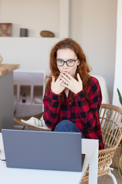 Jovem garota ruiva falando na cozinha usando um computador em casa