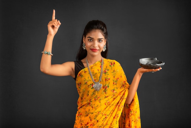 Jovem garota segurando e posando com utensílios de cozinha em um fundo cinza