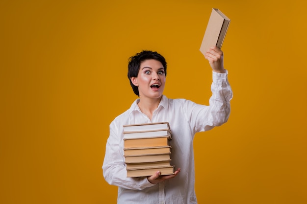 Foto jovem garota segurando muitos livros sobre um fundo amarelo