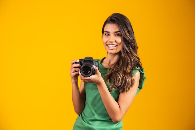 Jovem garota segurando uma câmera fotográfica em fundo amarelo. mulher tirando foto