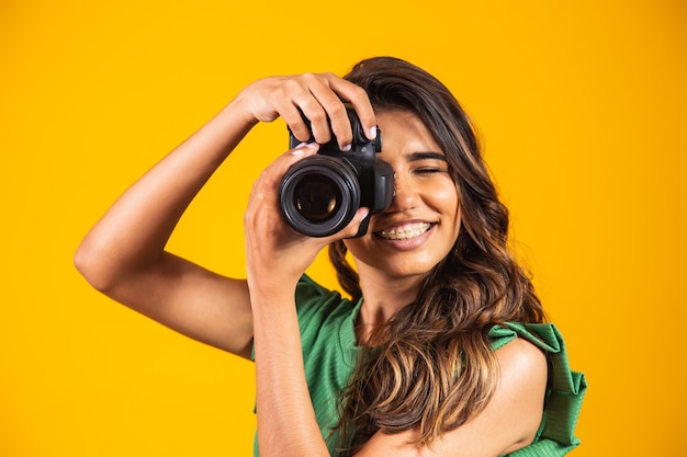 Jovem garota segurando uma câmera fotográfica em fundo amarelo. mulher tirando foto