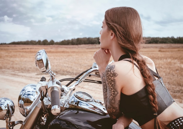 Jovem garota sexy, posando de motocicleta ao pôr do sol. Conceito de esporte a motor. Mídia mista