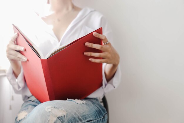 Jovem garota sexy sentada em estilo casual segura um livro com capa vermelha vazia nas mãos estilo de vida simulado