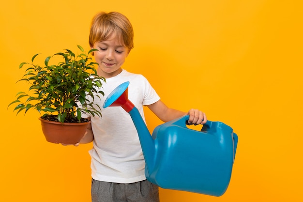 jovem garoto segurando uma panela com uma planta e um regador em uma parede laranja