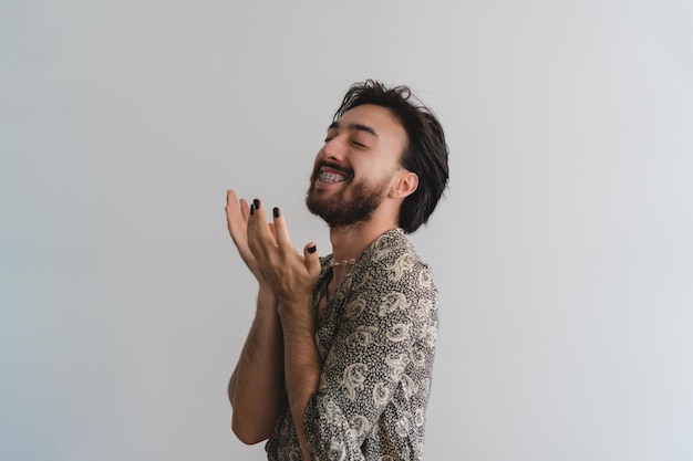 Jovem gay latino queer com um sorriso regozijando-se com os olhos fechados em um fundo branco