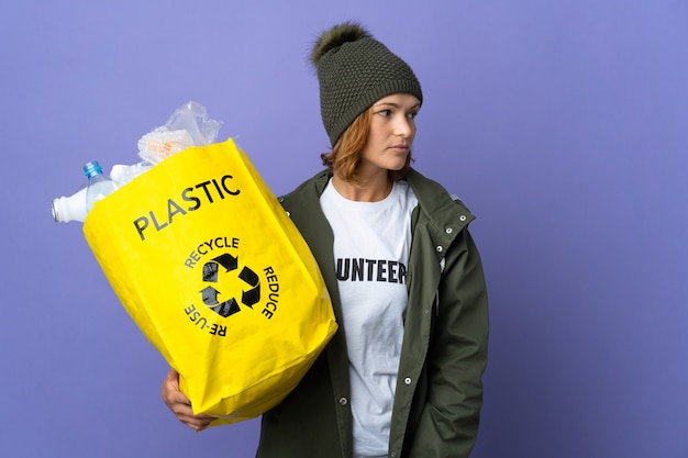 Jovem georgiana segurando uma sacola cheia de garrafas plásticas para reciclar olhando para o lado