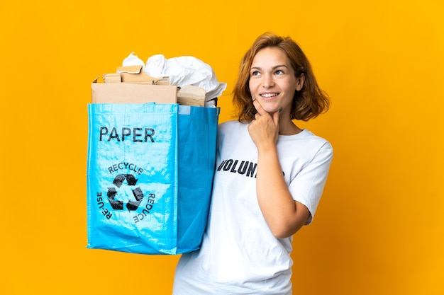 Jovem georgiana segurando uma sacola cheia de papel para reciclar olhando para cima enquanto sorri