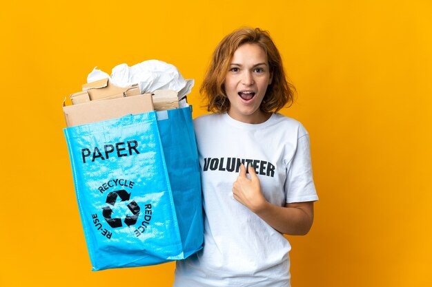 Jovem georgiana segurando uma sacola de reciclagem cheia de papel para reciclar com expressão facial surpresa