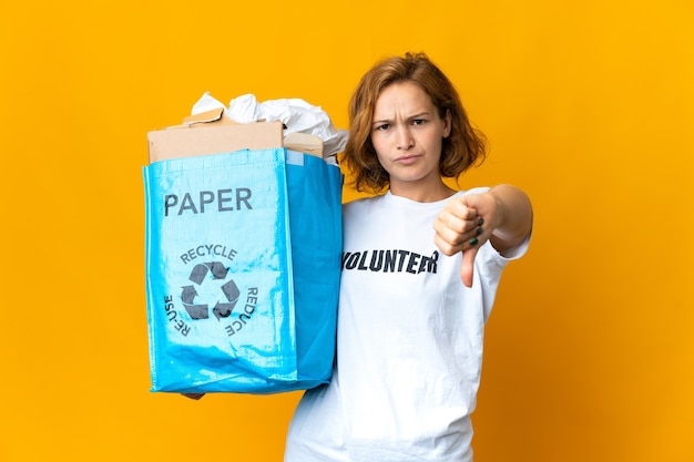 Jovem georgiana segurando uma sacola de reciclagem cheia de papel para reciclar, mostrando o polegar para baixo com expressão negativa