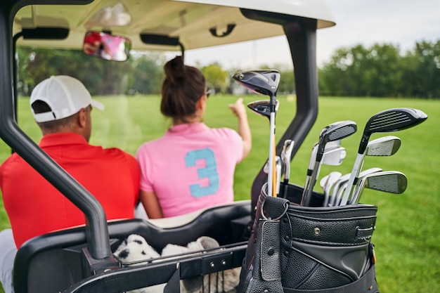 jovem golfista caucasiana de cabelos escuros apontando algo para um homem