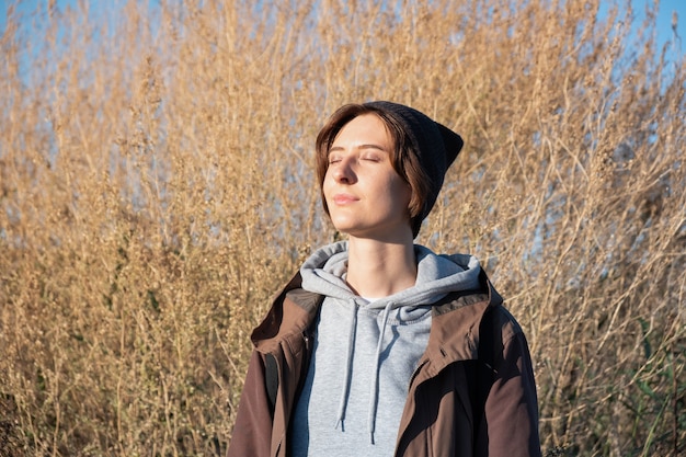 Jovem gosta do sol de outono. Mulher em parka ao ar livre em uma tarde ensolarada