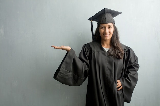 Jovem, graduado, indianas, mulher, contra, um, parede, segurando, algo, com, mãos, mostrando, um, produc