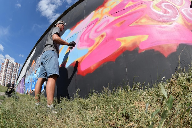 Jovem grafiteiro masculino caucasiano desenhando grande pintura de arte de rua em tons de azul e rosa