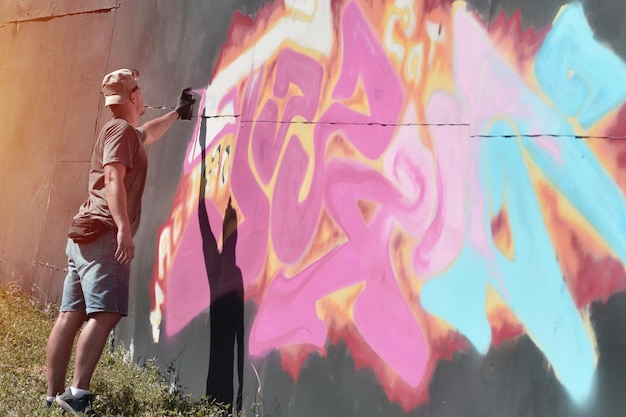 Jovem grafiteiro masculino caucasiano desenhando grande pintura de arte de rua em tons de azul e rosa