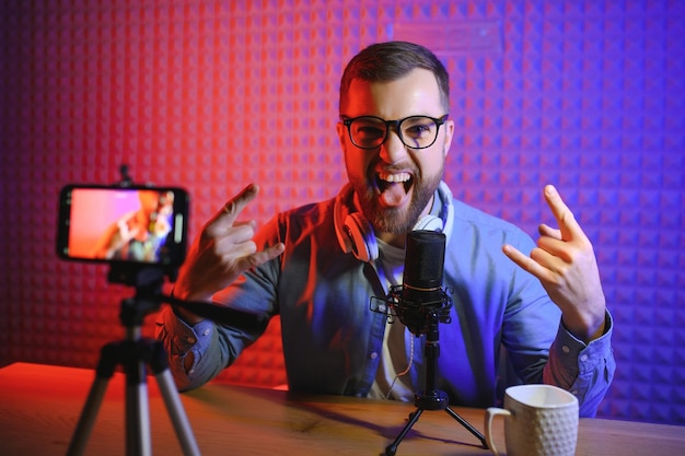 Jovem gravando ou transmitindo podcast usando microfone em seu pequeno estúdio de transmissão Criador de conteúdo