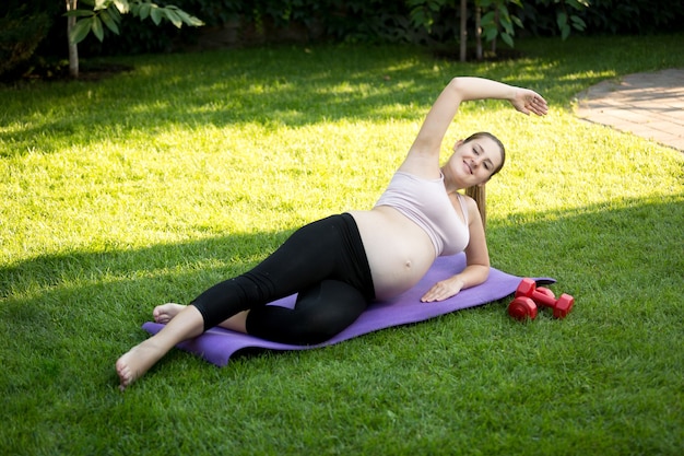 Foto jovem grávida alongando-se antes da ioga na grama do parque