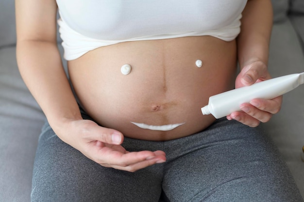 Jovem grávida aplicando creme hidratante nos cuidados de saúde da barriga e cuidados com a gravidez