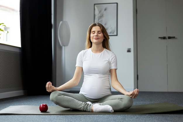 Jovem grávida atraente meditando fazendo ioga sentada em posição de lótus em casa Ioga para gravidez