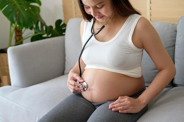 Jovem grávida colocando estetoscópio no conceito de cuidados de saúde e gravidez da barriga