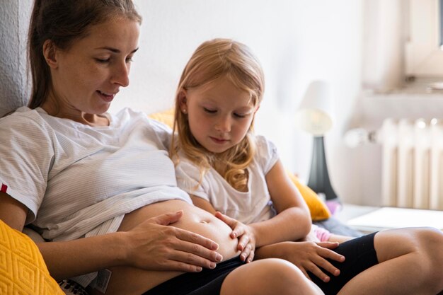 Jovem grávida com a filha ouvindo a batida do bebê