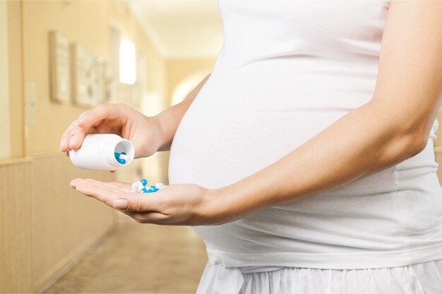 Jovem grávida com comprimidos em uma camiseta branca no fundo