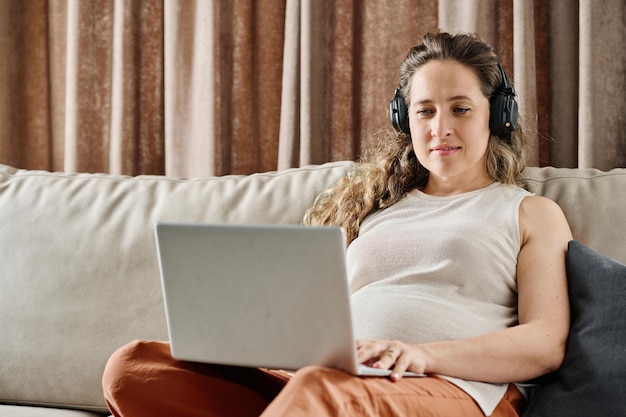 Jovem grávida com laptop de joelhos assistindo vídeo online