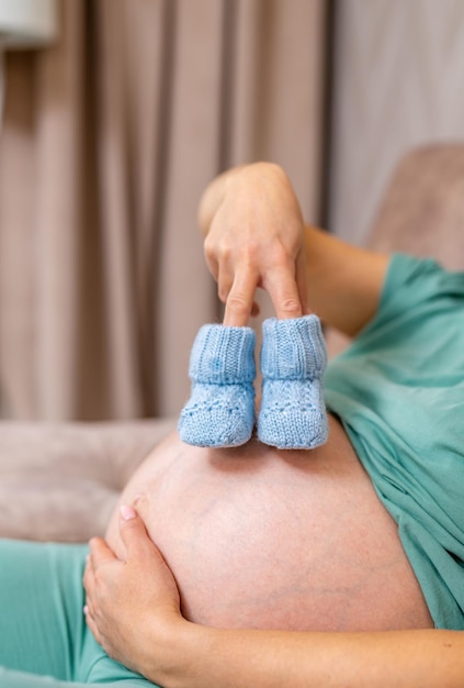 Jovem grávida com sapatos de bebê pequenos Sapatos minúsculos para o feto na barriga