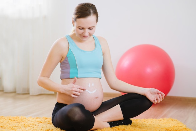 Jovem grávida desenha um sorriso pelo creme na barriga