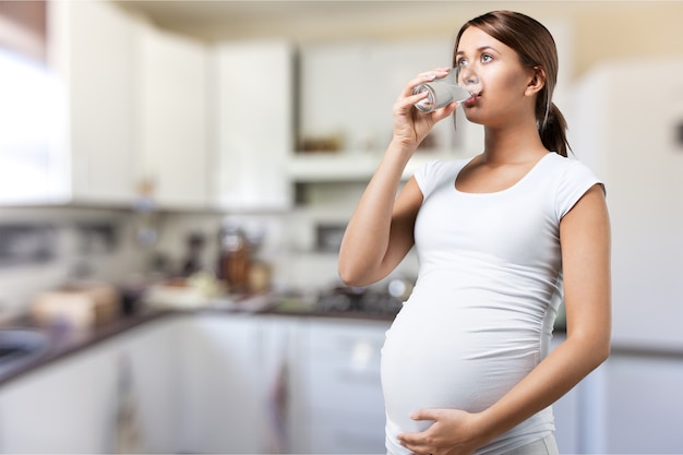 Jovem grávida em uma camiseta branca bebendo água no fundo