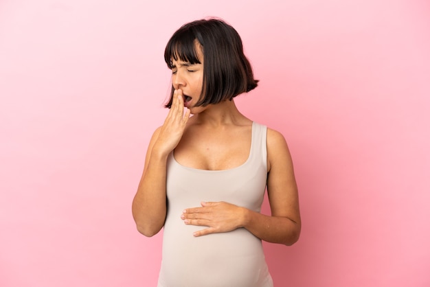 Jovem grávida em uma parede rosa isolada bocejando e cobrindo a boca aberta com a mão