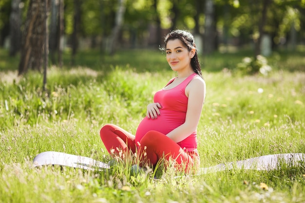 jovem grávida fazendo exercícios de ioga ao ar livre no parque.