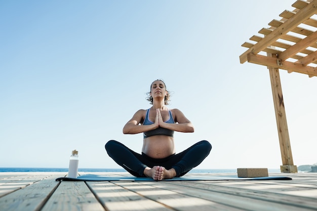 Jovem grávida fazendo ioga ao ar livre - conceito de meditação e maternidade para um estilo de vida saudável - foco no rosto