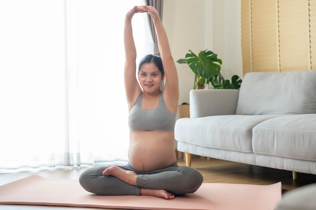 Jovem grávida fazendo ioga em casa conceito de cuidados de saúde e gravidez